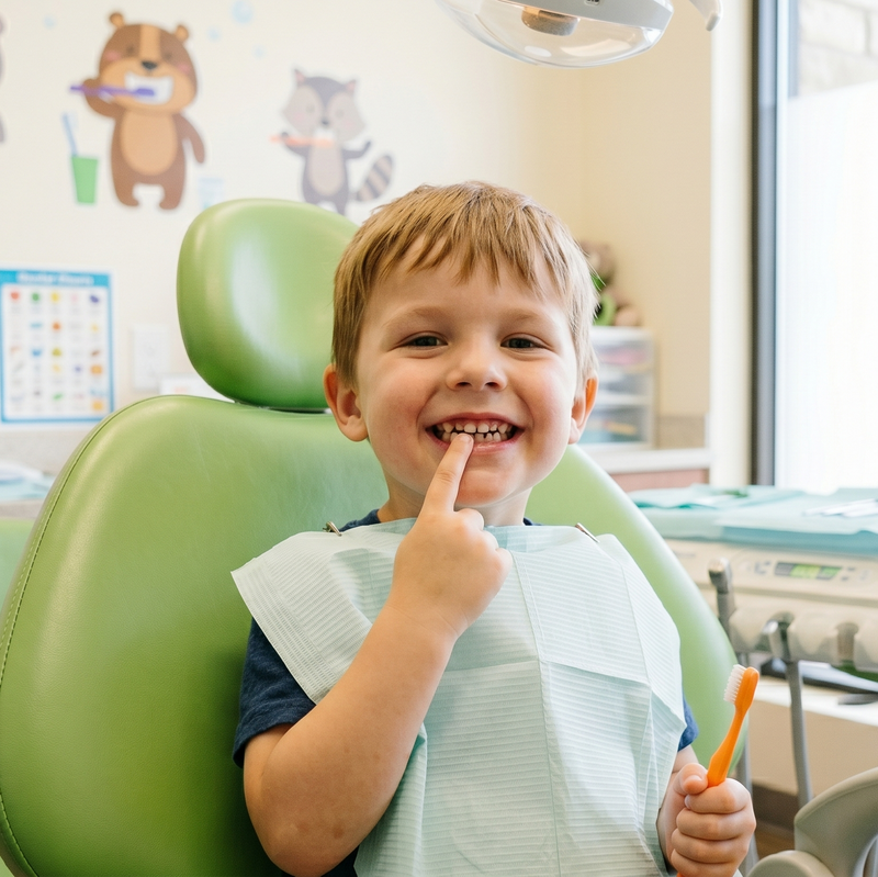 Child sitting in a green dentist chair with dental tools and equipment in the background