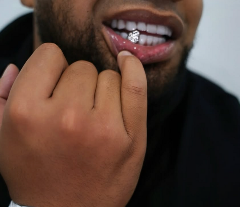 A close-up lifestyle shot of a man wearing a white Richard Millar watch and a silver diamond-encrusted lip ring, with his hand near his chin.